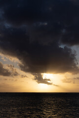 A golden sun setting over a tropical island reef featuring dark dramatic clouds in a moody sky.