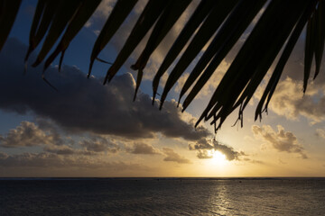 A golden sun sets over the shallow reefy shores of a tropical island.