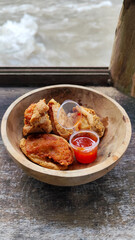 Tahu walik. Crispy browned tofu walik served in a natural wooden bowl with spicy chili sauce, with a blurry river flowing in the background. Menu at an outdoor cafe.