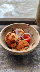 Tahu walik. Crispy browned tofu walik served in a natural wooden bowl with spicy chili sauce, with a blurry river flowing in the background. Menu at an outdoor cafe.