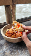 Tahu walik. Crispy browned tofu walik served in a natural wooden bowl with spicy chili sauce, with a blurry river flowing in the background. Menu at an outdoor cafe.