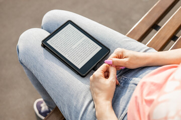 woman reading e-book sitting on bench, close-up. an e-book lies on a girl's lap. ebook mockup. 
