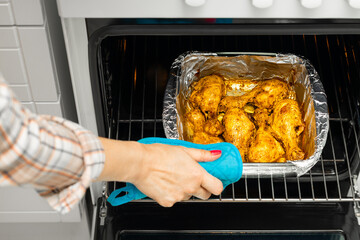 housewife takes fried chicken legs out of the oven. cooking chicken legs at home. cooking chicken legs in the oven. chicken in foil