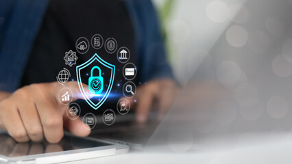 Close-up of a hand using a digital tablet with a cybersecurity shield icon surrounded by data...