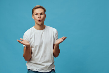 Confused young man with puzzled expression, wearing casual white t-shirt, gesturing with palms up,...