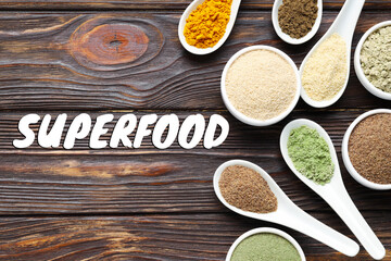 Superfood. Different powders in bowls and spoons on wooden table, flat lay