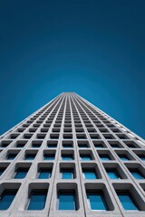 Looking up at a modern concrete building with repeating square windows against a clear blue sky, creating a geometric pattern