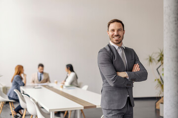 Portrait of confident businessman standing at boardroom with arms crossed during the meeting at...