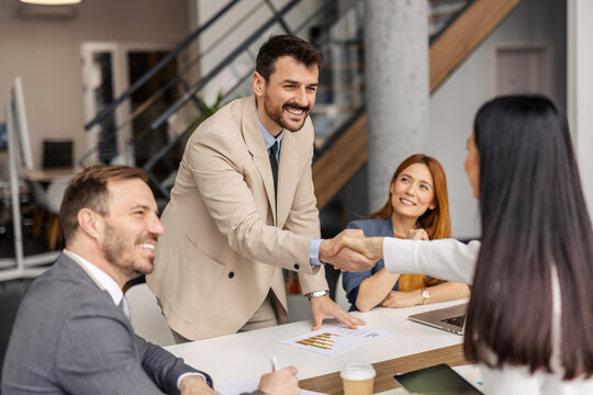 Happy manager shaking hands with new employee at corporate firm.