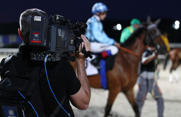 Operador de cámara de televisión grabando con cámara al hombro a un caballo y su jockey en el hipódromo © Diego