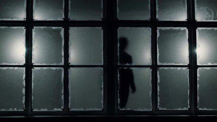 A scary silhouetted figure stands by a window with frosted glass. Copy space halloween scary background