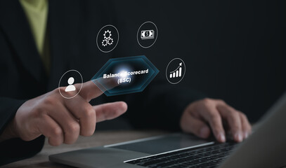 Businessman using a digital interface to select 'Balance Scorecard (BSC)' on a laptop, surrounded by icons representing finance, growth, operations, and human resources in strategic planning.