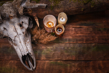 Deer skull, burning candles, log with moss on old mystical wizard table background.