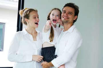 Father and mother are hugging their smiling daughter as they stand in front of the house.