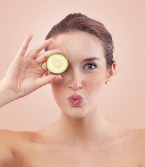 Woman blowing a kiss while covering her eyes with cucumber slices, showing natural skin with acne...