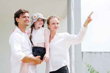 Father and mother are hugging their smiling daughter as they stand in front of the house.