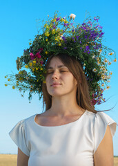 Portrait of a girl in a white dress, Slavic appearance with a wreath of wild flowers on her head.