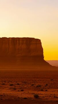 Desert mesa rock formation stands silhouetted against dramatic golden hour sky transitioning from purple twilight to warm orange sunrise creating stunning southwestern landscape