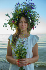 Portrait of a girl in a white dress, Slavic appearance with a bouquet and wreath of wild flowers on...