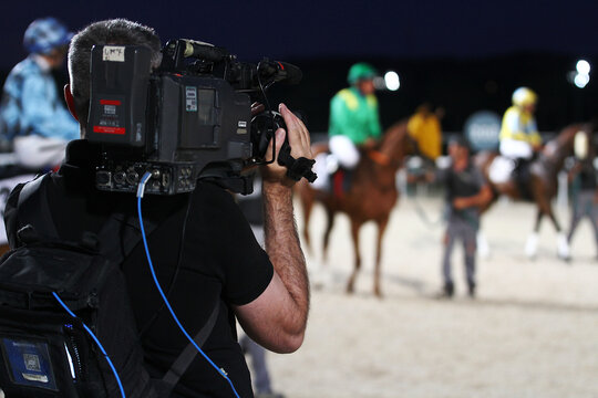Camar&oacute;grafo TV en cajones de salida grabando una carrera de caballos en el hip&oacute;dromo con c&aacute;mara audiovisual profesional al hombro