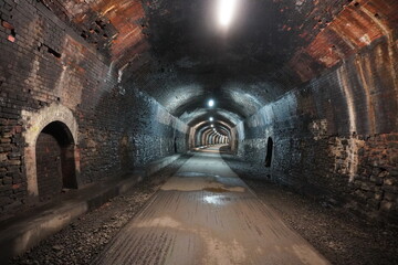 Historic brick railway tunnel with lights and wet gravel path in The Peak District, England.