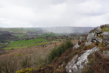 Scenic misty green valley and rocky outcrop view over rolling hills in The Peak District, England.