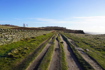Rugged dirt track beside stone wall on sunny moorland hill in The Peak District, England.
