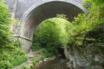 Stone railway viaduct crossing forest stream and fern-covered gorge in The Peak District, England.