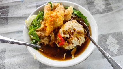 Bakso. A complete bowl of meatballs with yellow noodles, crispy fried dumplings and fresh green vegetables served with delicious, rich sauce on the table.