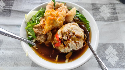 Bakso. A complete bowl of meatballs with yellow noodles, crispy fried dumplings and fresh green vegetables served with delicious, rich sauce on the table.
