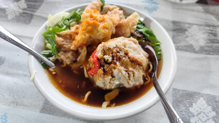Bakso. A complete bowl of meatballs with yellow noodles, crispy fried dumplings and fresh green vegetables served with delicious, rich sauce on the table.