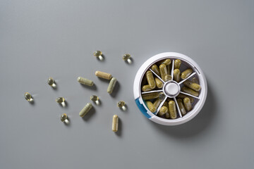 Colorful dietary capsules arranged around a stylish weekly pill organizer on a sleek grey surface