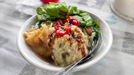 Bakso. A complete bowl of meatballs with yellow noodles, crispy fried dumplings and fresh green vegetables served with delicious, rich sauce on the table.