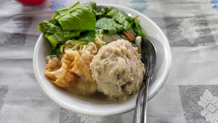 Bakso. A complete bowl of meatballs with yellow noodles, crispy fried dumplings and fresh green vegetables served with delicious, rich sauce on the table.