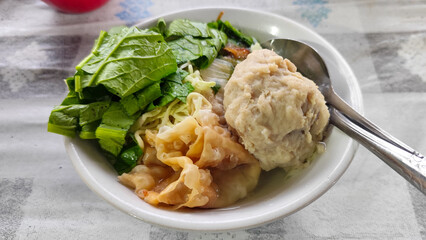 Bakso. A complete bowl of meatballs with yellow noodles, crispy fried dumplings and fresh green vegetables served with delicious, rich sauce on the table.