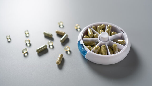 Capsules and supplements arranged on a gray surface with a weekly organizer highlighting a health-focused lifestyle