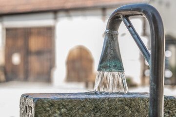 Detail fließender  Brunnen mit gebogenem Brunnenrohr aus Kupfer mit Grünspan vor altem unscharfem...