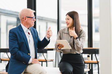 Businessman in blue suit and woman in gray shirt having cheerful discussion in modern office, holding tablet, teamwork and collaboration concept