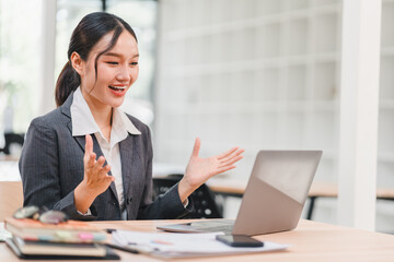 Young Asian businesswoman in gray suit smiling and gesturing during video call at modern office...