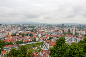 An expansive elevated view captures the cityscape of Ljubljana, on a cloudy day. Red-tiled rooftops...