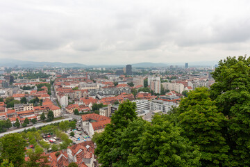 An expansive elevated view captures the cityscape of Ljubljana, on a cloudy day. Red-tiled rooftops...