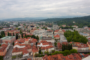 Fototapeta premium An expansive elevated view captures the cityscape of Ljubljana, on a cloudy day. Red-tiled rooftops dominate the foreground, showcasing the charming historic architecture of the old town
