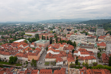 Obraz premium An expansive elevated view captures the cityscape of Ljubljana, on a cloudy day. Red-tiled rooftops dominate the foreground, showcasing the charming historic architecture of the old town