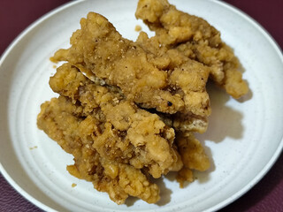 A plate of crispy golden fried chicken fillet, served on a blurred background.