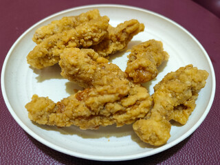 A plate of crispy golden fried chicken fillet, served on a blurred background.