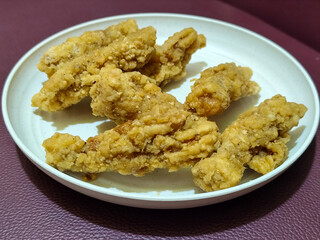 A plate of crispy golden fried chicken fillet, served on a blurred background.