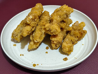 A plate of crispy golden fried chicken fillet, served on a blurred background.