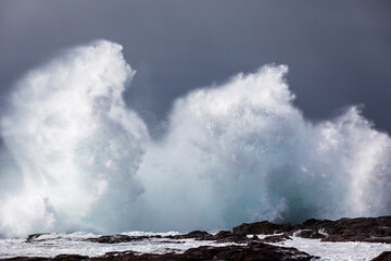 A huge ocean wave curls and breaks onto a rocky headland, exploding into a wall of white water...
