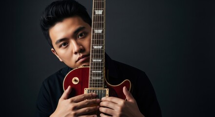 Obraz premium Young asian male holding electric guitar against dark background