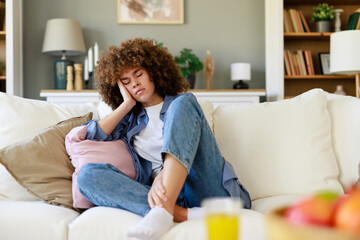 Curly-Haired Woman Feeling Unwell on Sofa in Cozy Living Room with Warm Decor